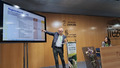 A speaker is presenting at a podium with a large screen displaying a slide titled "Regenerative Measures." The slide outlines practices and strategies related to regenerative agriculture. The podium is branded with the event's theme, "Cultivating the Future: Organic and Regenerative Action," and decorated with a floral arrangement. The venue branding "IFEZA" and "Diputación Zamora" is visible on the wooden wall behind the speaker, emphasizing the event's location and organizers.