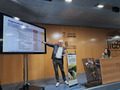 A speaker is presenting at a podium with a large screen displaying a slide titled "Regenerative Measures." The slide outlines practices and strategies related to regenerative agriculture. The podium is branded with the event's theme, "Cultivating the Future: Organic and Regenerative Action," and decorated with a floral arrangement. The venue branding "IFEZA" and "Diputación Zamora" is visible on the wooden wall behind the speaker, emphasizing the event's location and organizers.